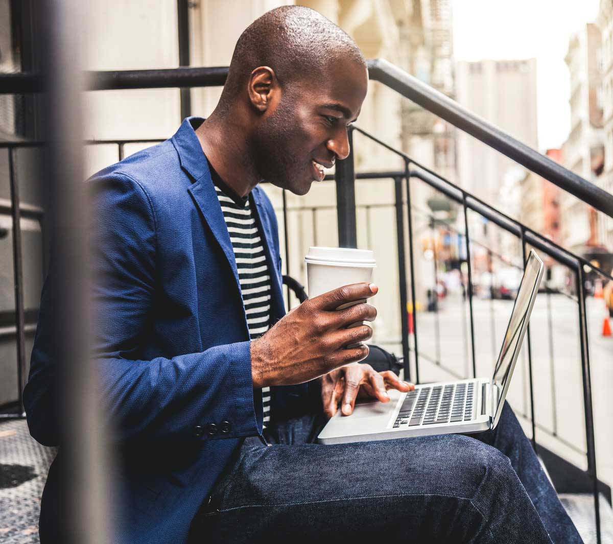 Un tipo revisando su correo electrónico y bebiendo café al aire libre en unas escaleras